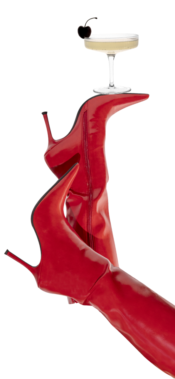 Roter High-Heel-Stiefel balanciert ein Champagnerglas mit Kirsche